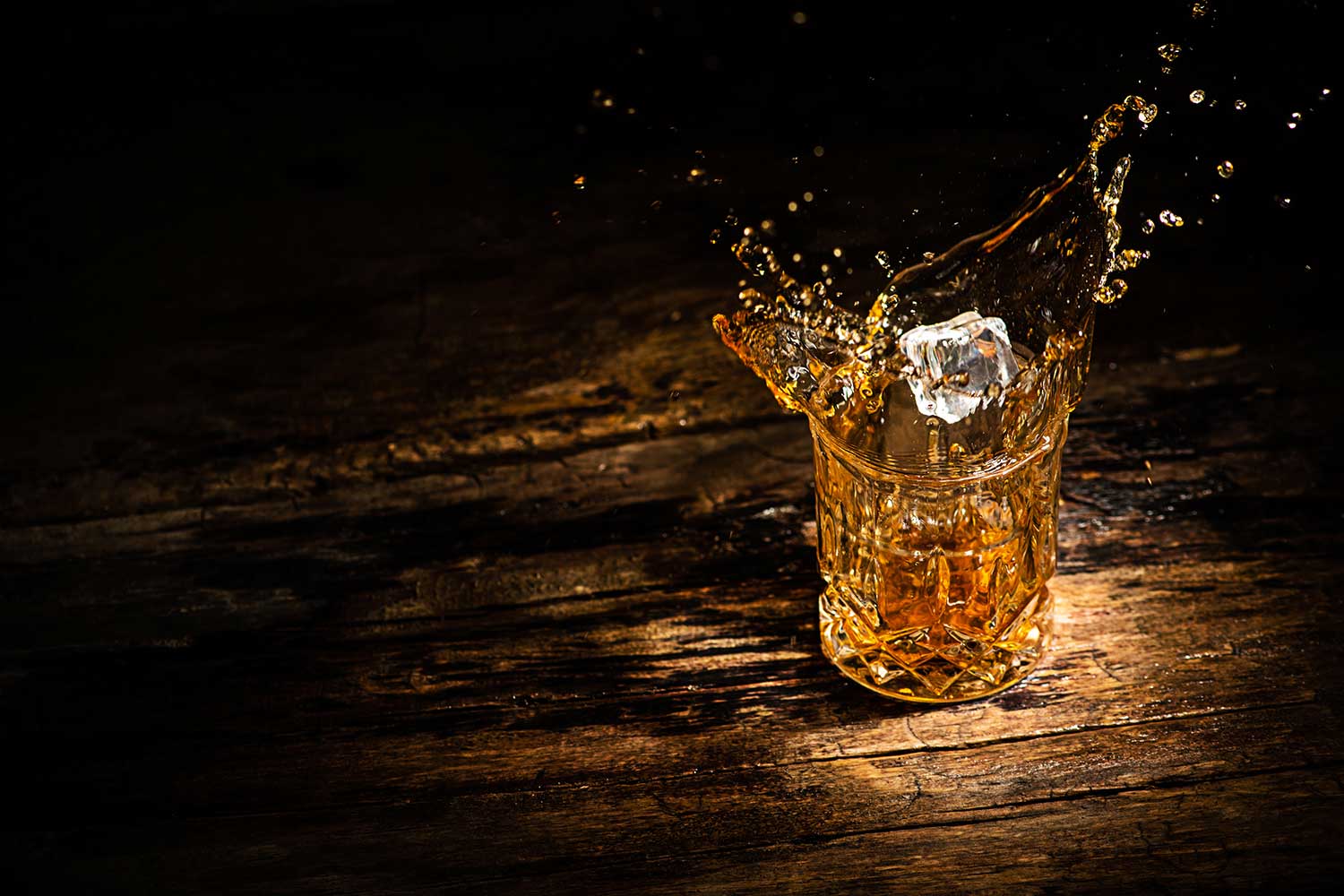 glass with whisky with splashes from ice cube on a wooden background